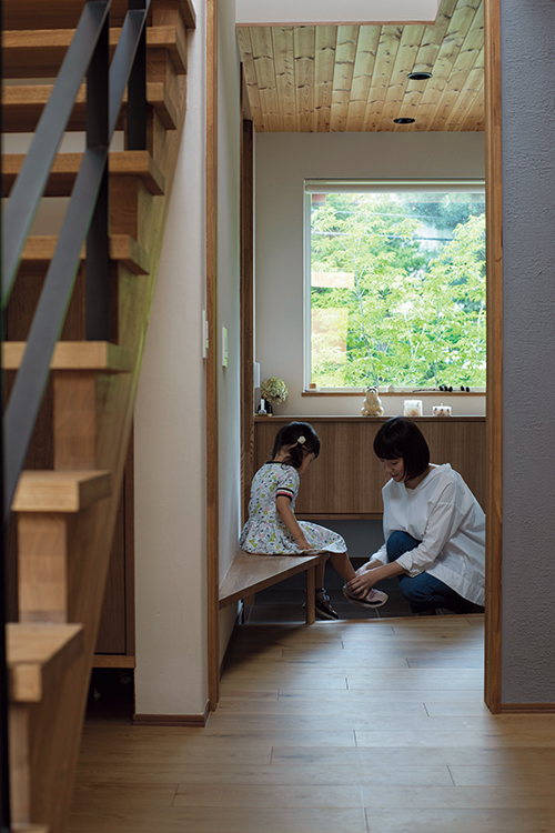 リビングから見た玄関。窓からは近隣の緑が見える。造作のベンチは、お子さんに靴を履かせたり、荷物を置くのに便利